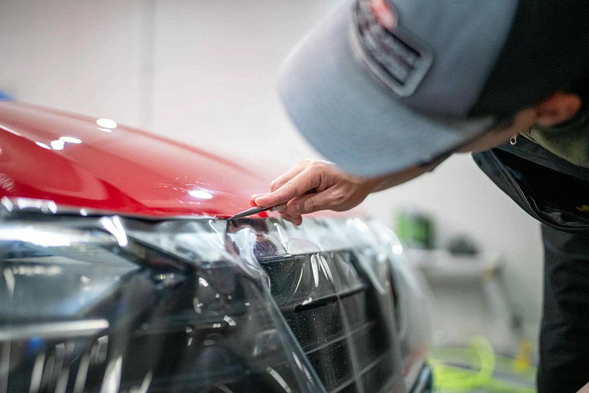 A man is covering the hood of a red car with plastic wrap.