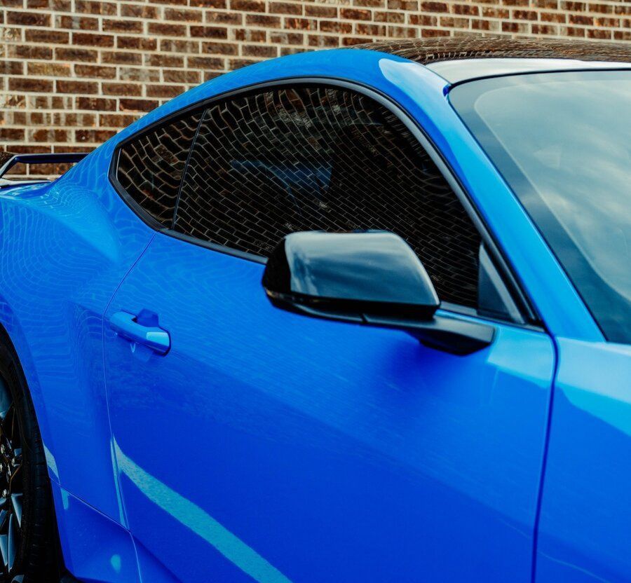 A blue car with a tinted window is parked in front of a brick wall.