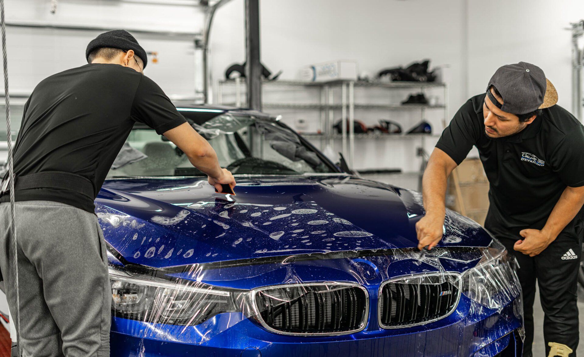 Two men are wrapping a blue car with plastic wrap.