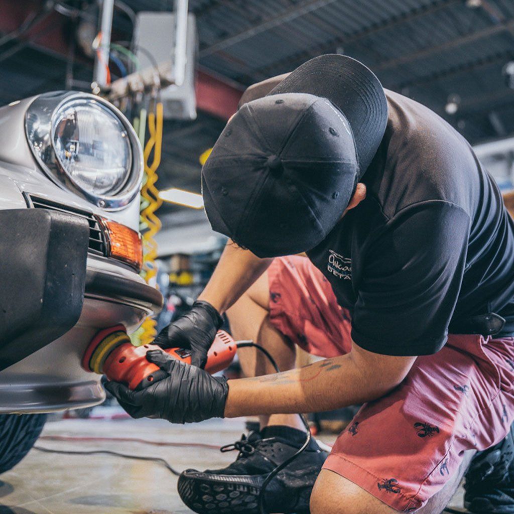 A man is polishing the front of a car in a garage.