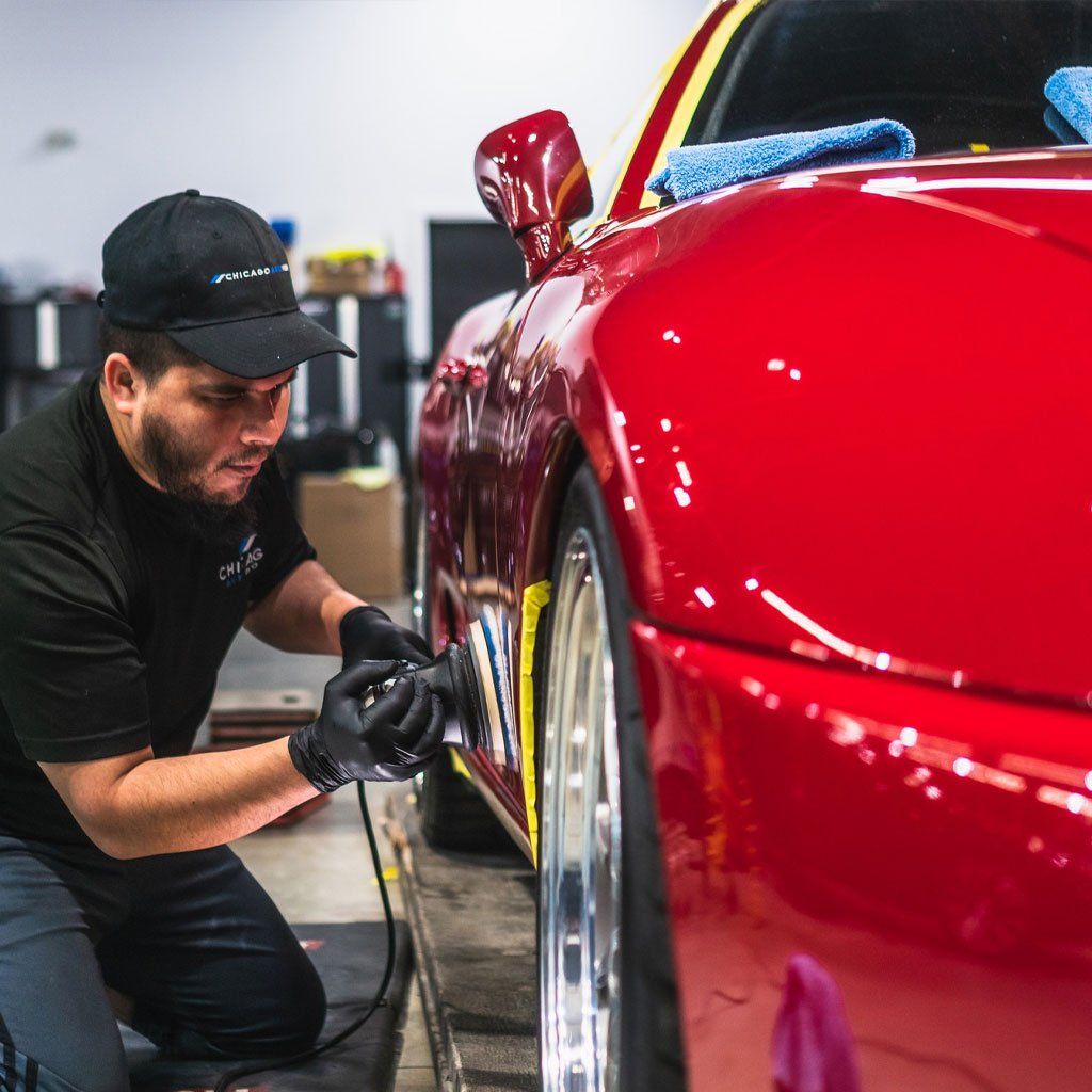 A man is polishing the side of a red sports car.