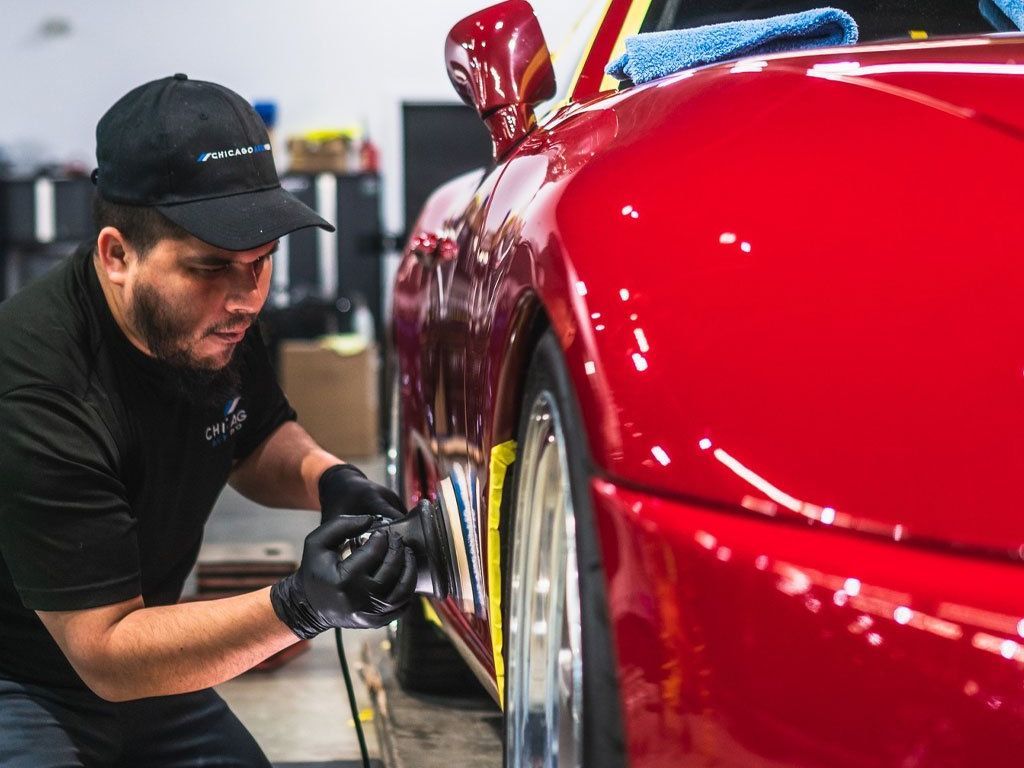 A man is polishing the side of a red sports car.