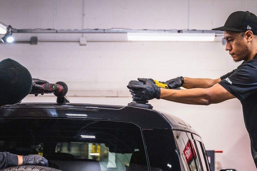 A man is working on the roof of a car in a garage.