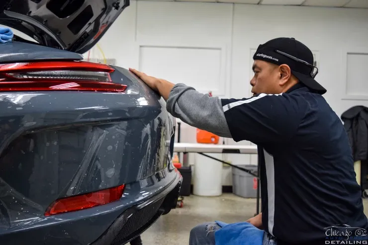 A man is applying a protective film to the back of a car.
