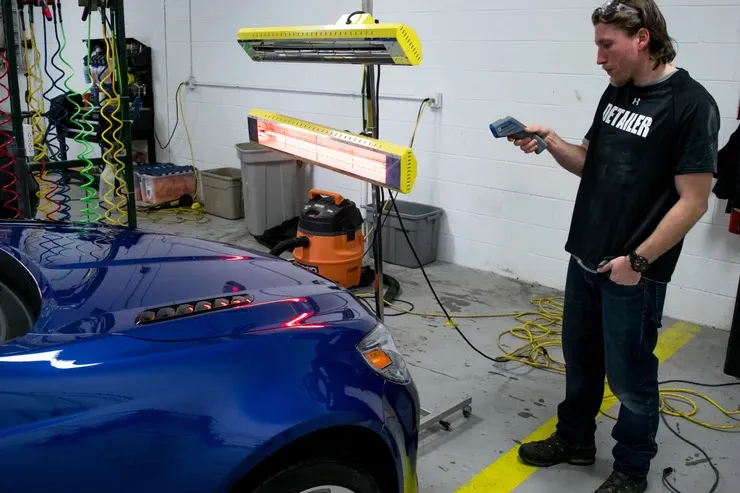 A man wearing a shirt that says fender is standing next to a blue car
