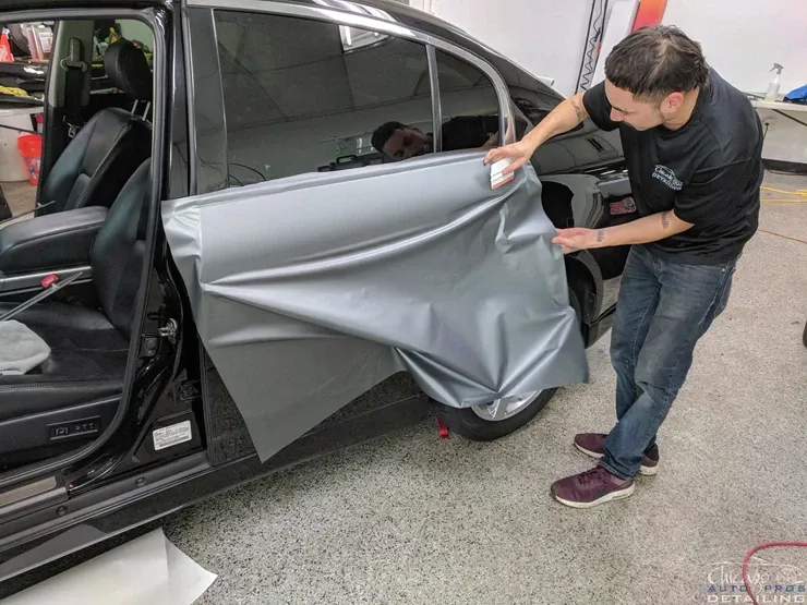 A man is wrapping a car door with a piece of wrapping paper.