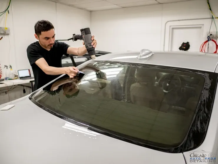 A man is working on a car windshield in a garage.