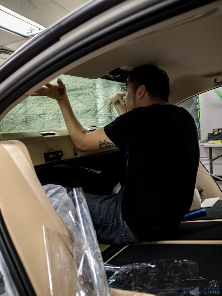 A man is sitting in the driver 's seat of a car applying window tinting.