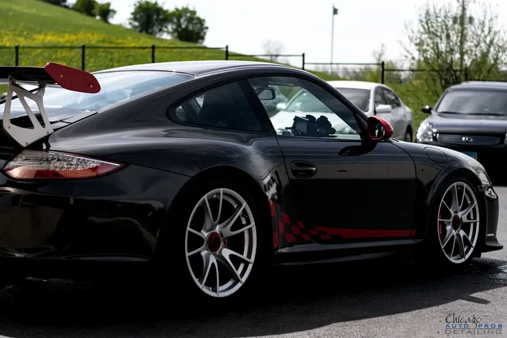 A black porsche is parked in a parking lot with other cars