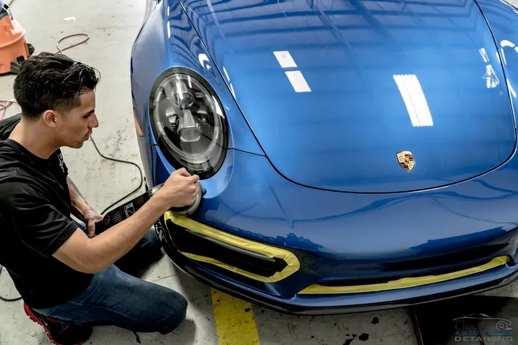 A man is kneeling down in front of a blue porsche 911.