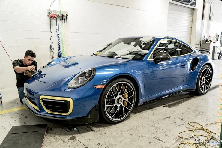 A man is working on a blue porsche 911 turbo s in a garage.