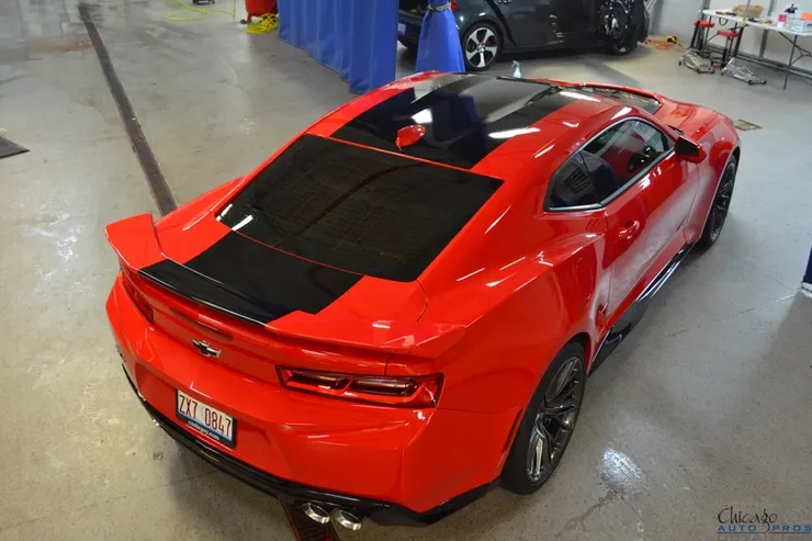 A red car with a black stripe on the side is parked in a garage
