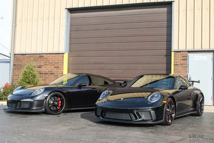 Two black sports cars are parked in front of a garage door.