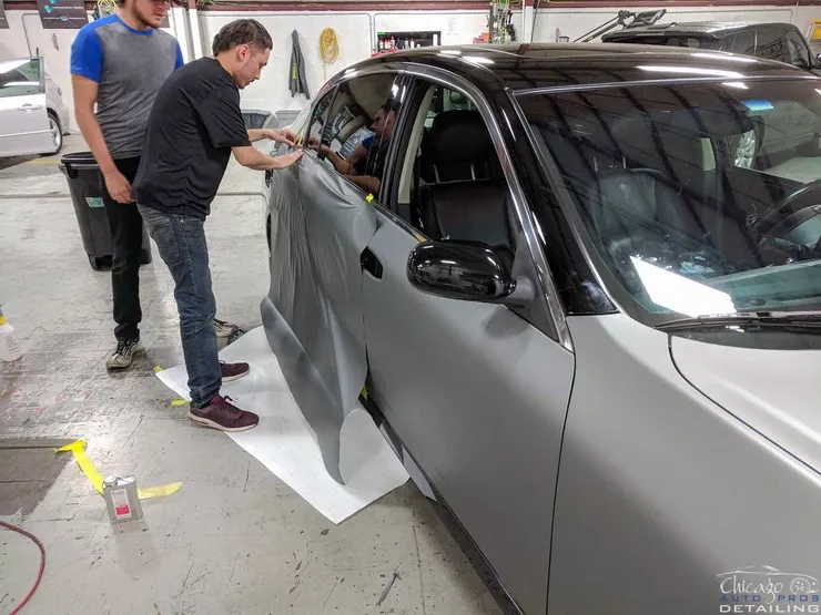 Two men are wrapping a car in a garage.