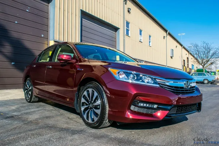 A red honda accord hybrid is parked in front of a building.