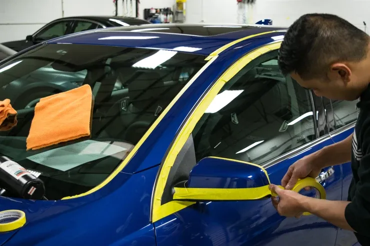 A man is applying yellow tape to a blue car