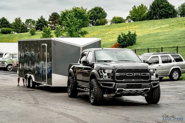 A black ford raptor truck is towing a trailer in a parking lot.