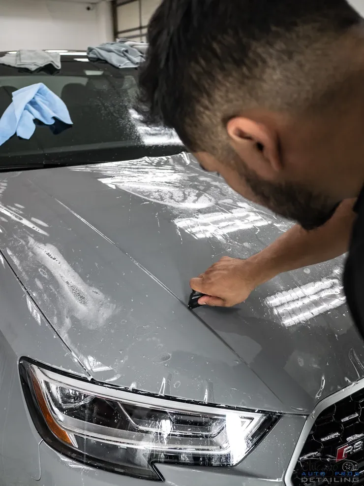 A man is applying a protective film to the hood of a car.