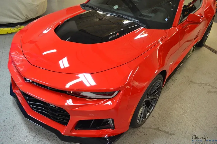 A red car with a black hood is parked in a garage