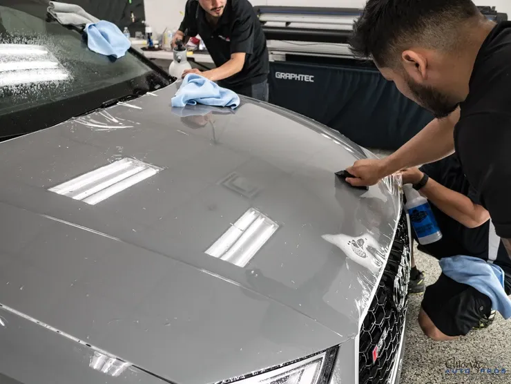 Two men are cleaning the hood of a car in a garage.
