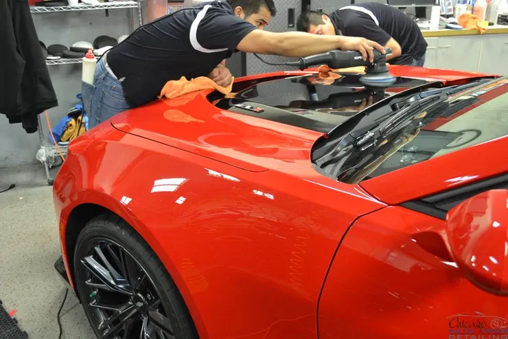 Two men are polishing the hood of a red car