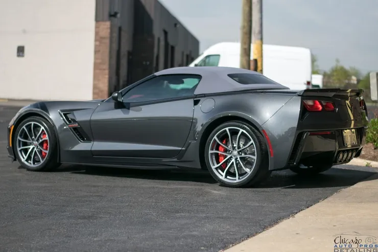 A gray sports car is parked in a parking lot in front of a building.