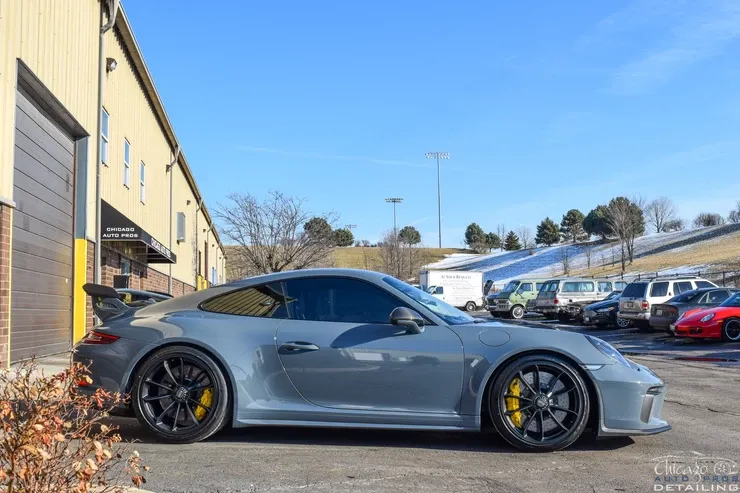 A grey porsche 911 gt3r is parked in a parking lot in front of a building.