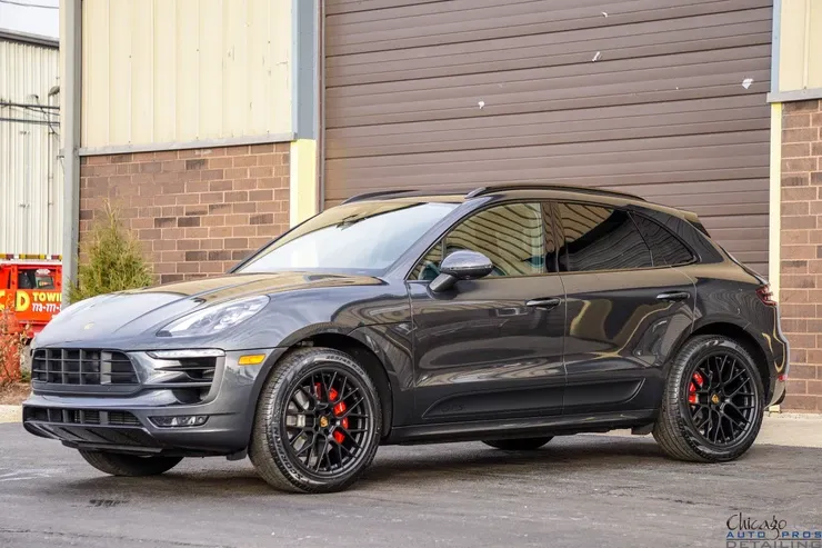 A gray porsche macan turbo is parked in front of a brick building.