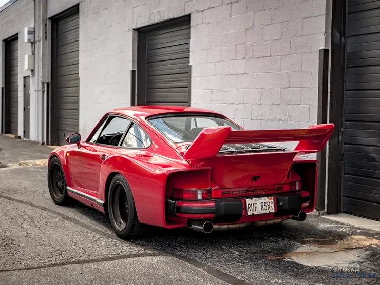 A red porsche is parked in front of a garage.