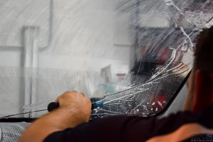 A man is cleaning a car windshield with a screwdriver.
