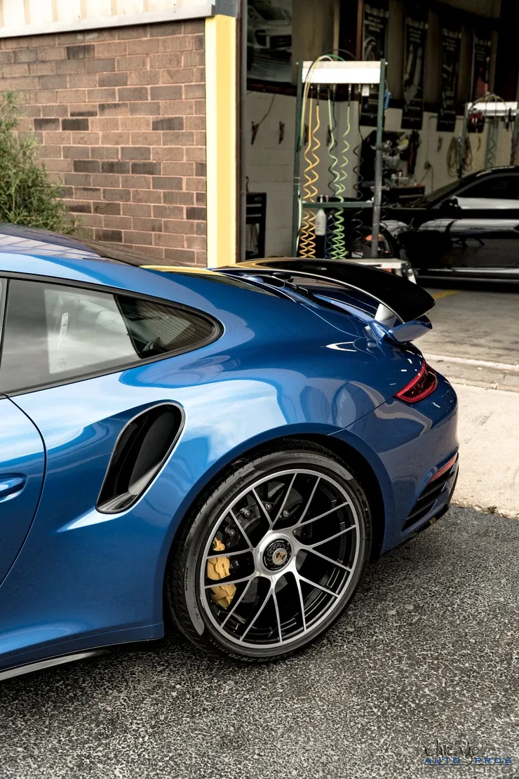 A blue porsche 911 turbo s is parked in front of a garage.
