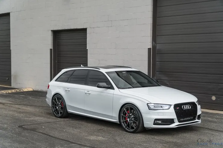 A white audi a4 station wagon is parked in front of a garage door.