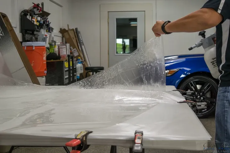 A man is spraying a piece of plastic on a table in a garage.