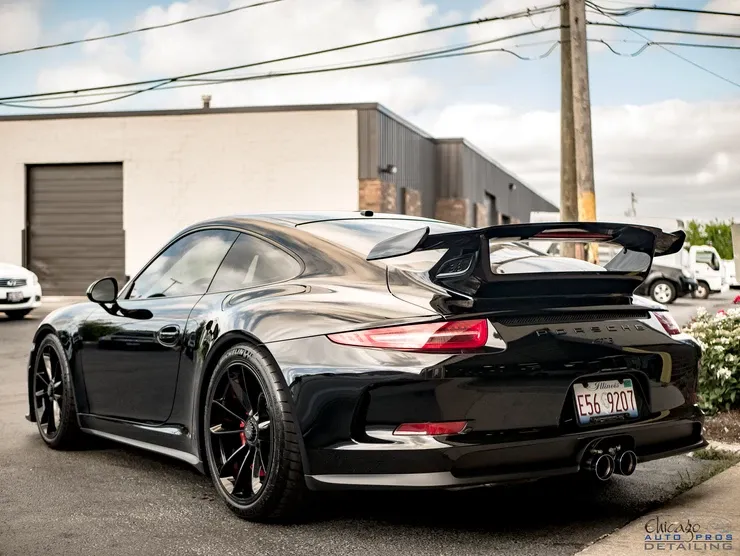 A black porsche 911 gt3 is parked in front of a building.