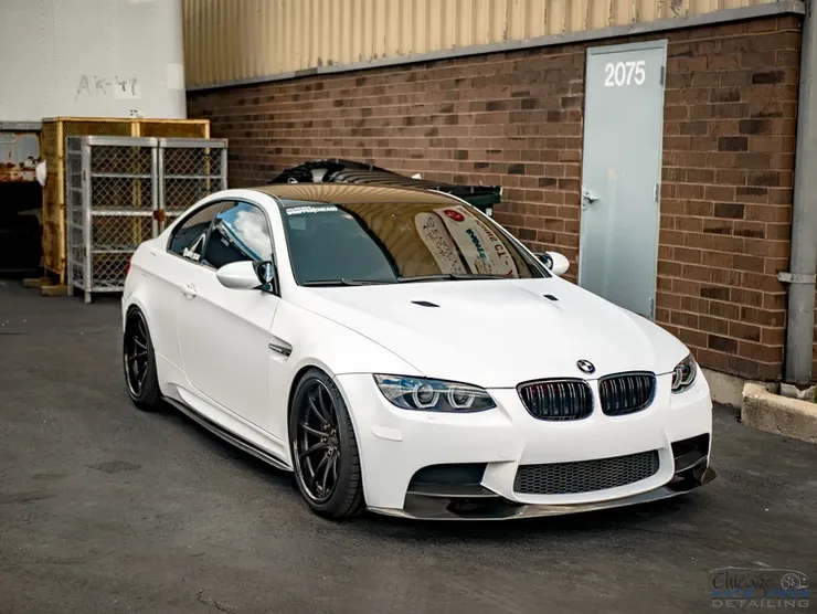 A white bmw m3 is parked in front of a brick building.