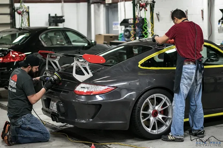 Two men are polishing a gray sports car in a garage.