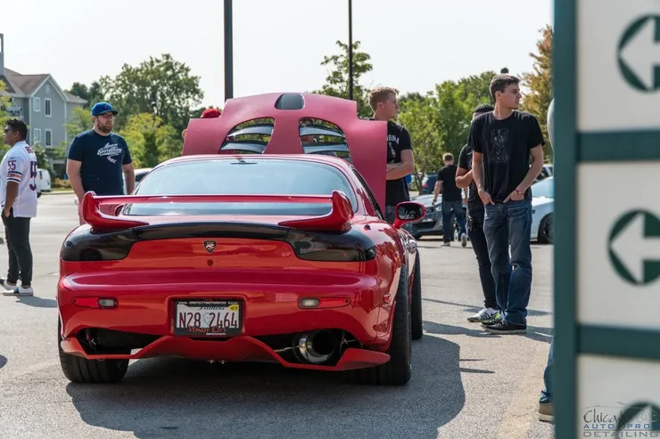 A group of people are standing around a red sports car with the hood up.
