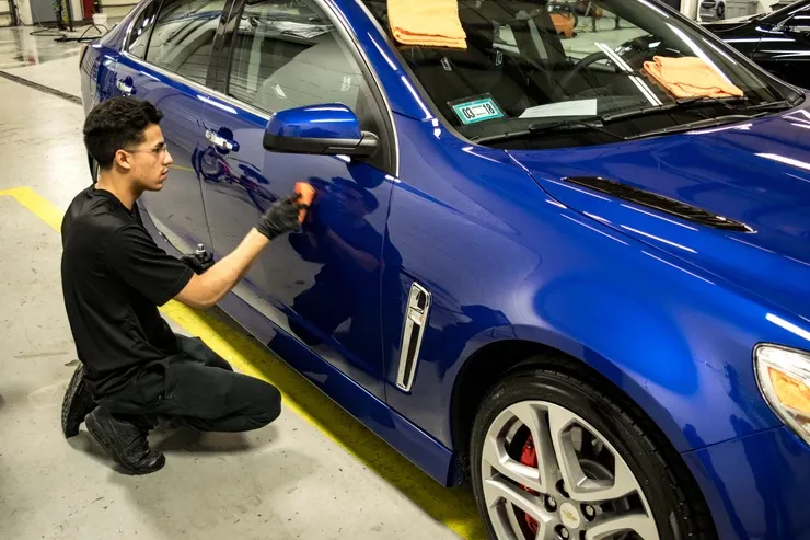 A man is kneeling down next to a blue car in a garage.