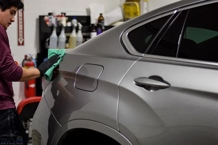 A man is cleaning a car with a cloth in a garage.