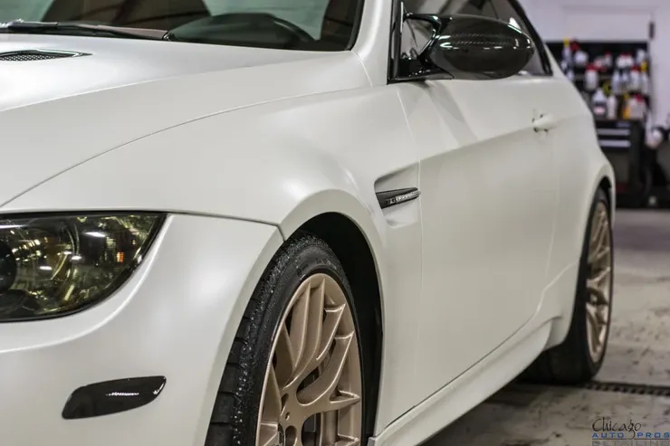 A white car with gold wheels is parked in a garage.