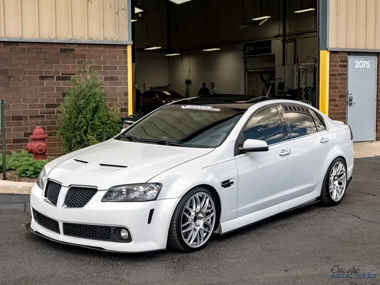 A white pontiac gto is parked in front of a brick building.