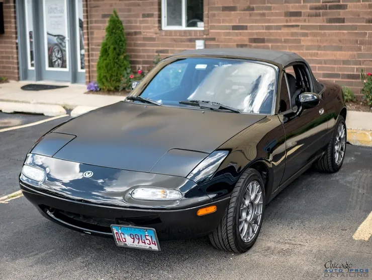 A black sports car is parked in a parking lot in front of a brick building.