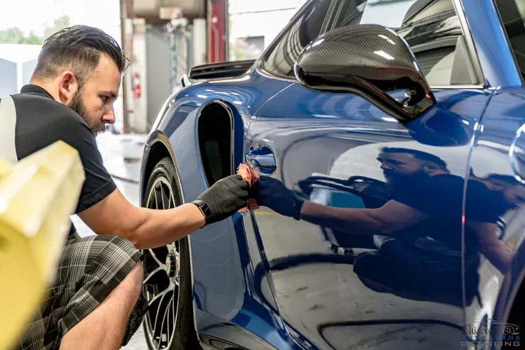 A man is polishing the side of a blue sports car.