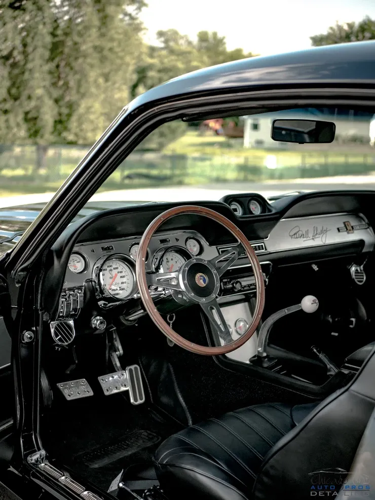 The interior of a black mustang with a wooden steering wheel and dashboard.