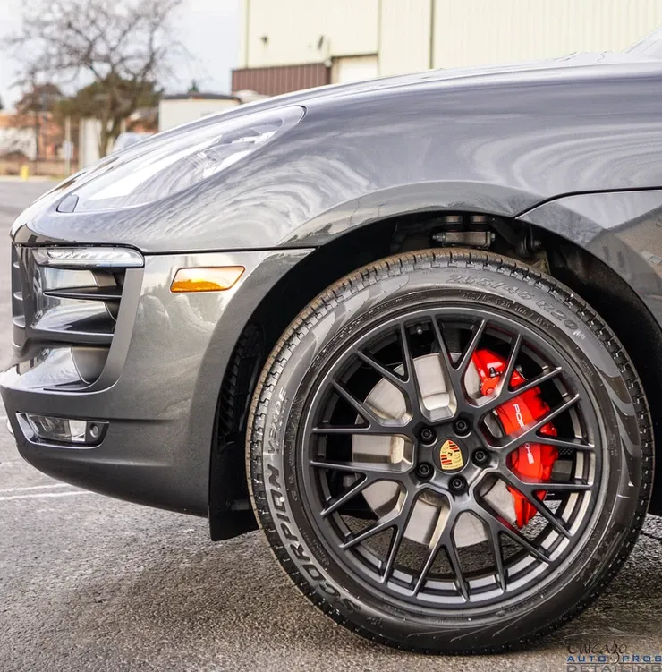 A black car with a red brake caliper is parked in a parking lot