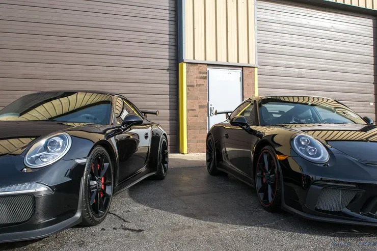 Two black sports cars are parked next to each other in front of a garage door.