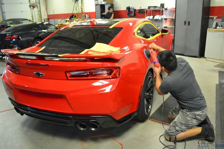 A man is polishing a red car in a garage