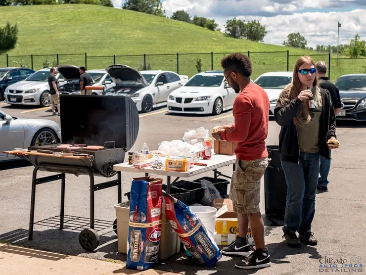A man is standing next to a table with a grill in a parking lot.