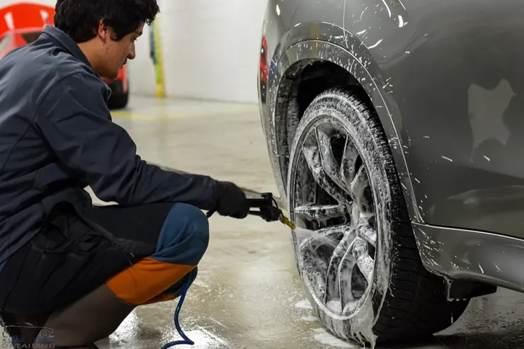 A man is kneeling down to wash the wheels of a car