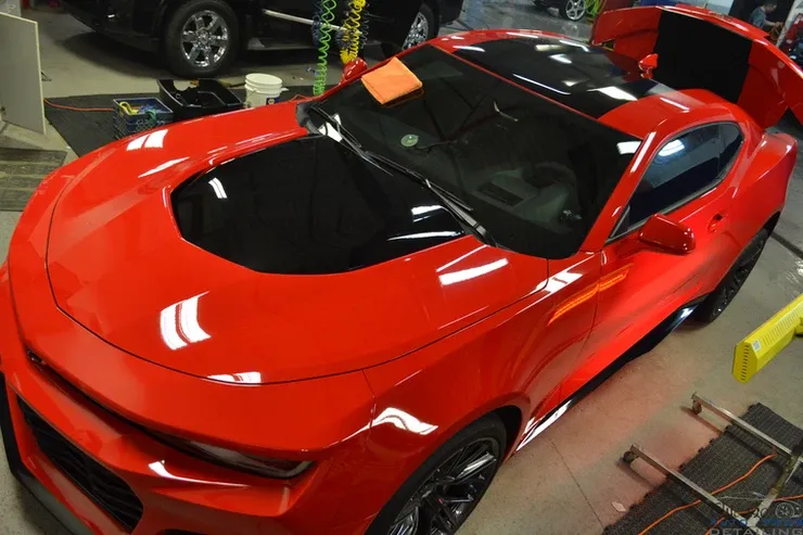 A red car with a black hood is parked in a garage